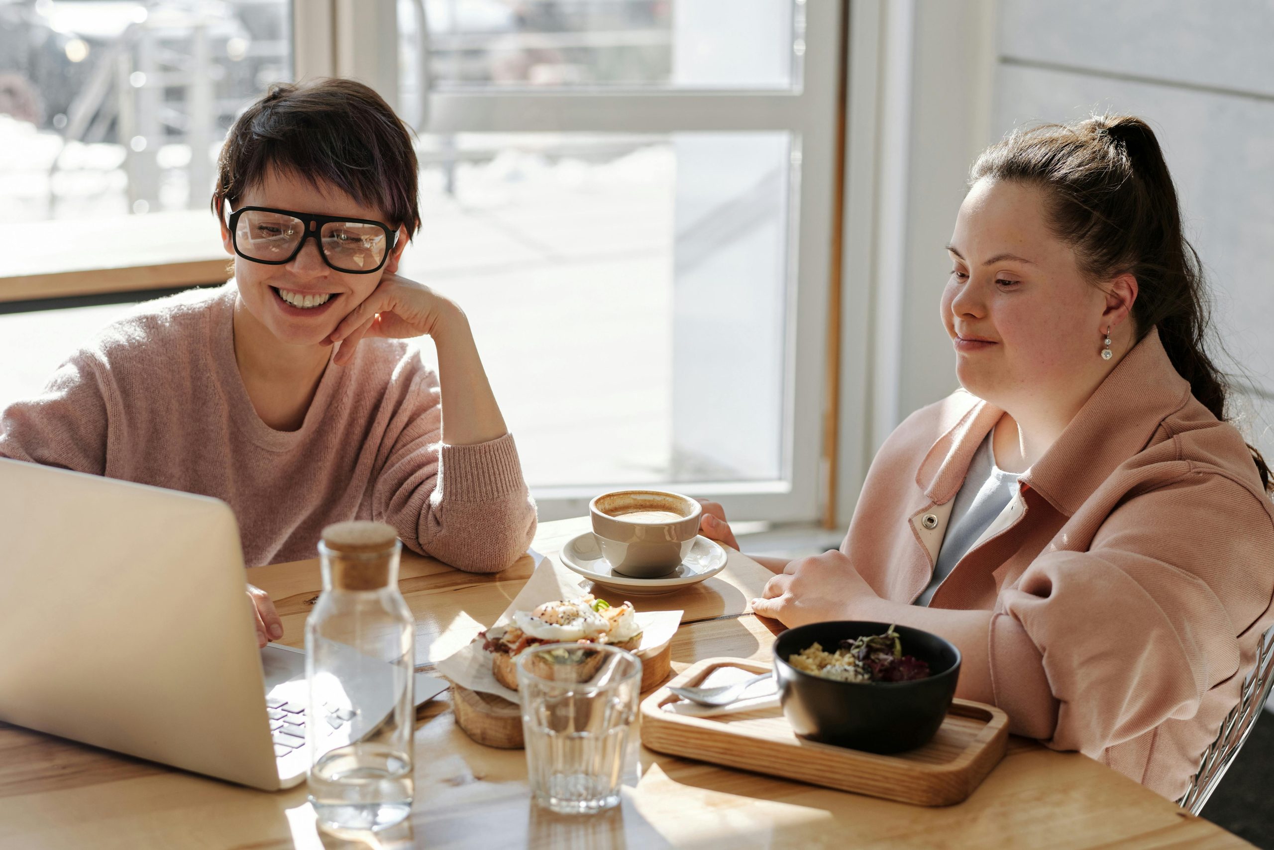 Two cheerful women enjoying coffee and food in a bright, modern indoor setting.