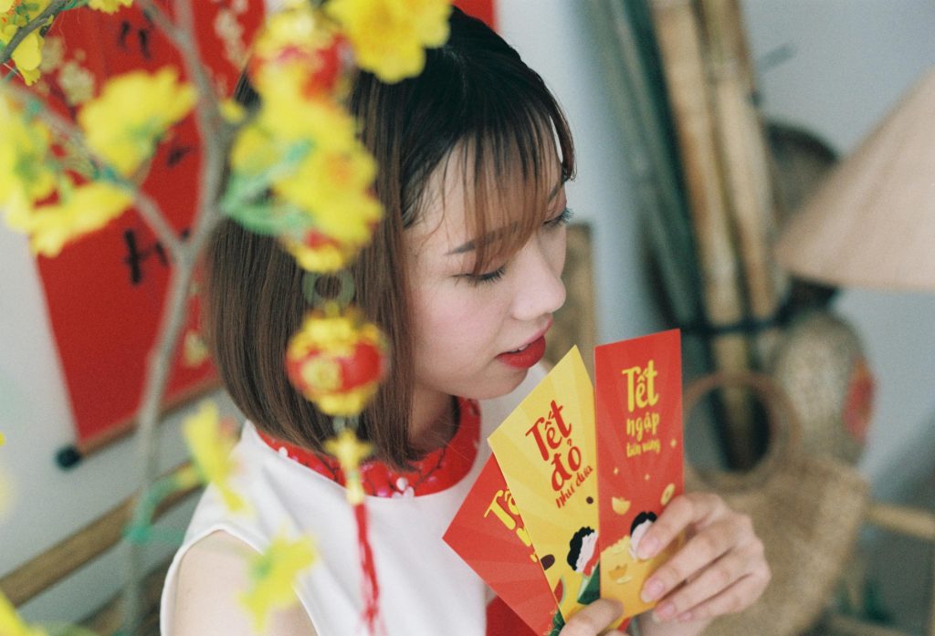 Woman holding lucky envelopes during Vietnamese Lunar New Year celebration with traditional decor.